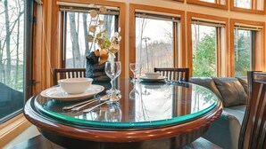 A dining area with a round glass table, wooden chairs, and a vase with flowers. - Slopeside Boyne Mtn Resort Condo w/ Deck! (Boyne Falls)