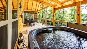 Eine Holzterrasse mit Whirlpool, Gartenmöbeln und Blick auf den Wald.