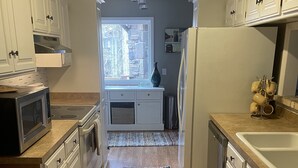 A kitchen with white cabinets, a microwave, a refrigerator, and a window with a view of trees.
