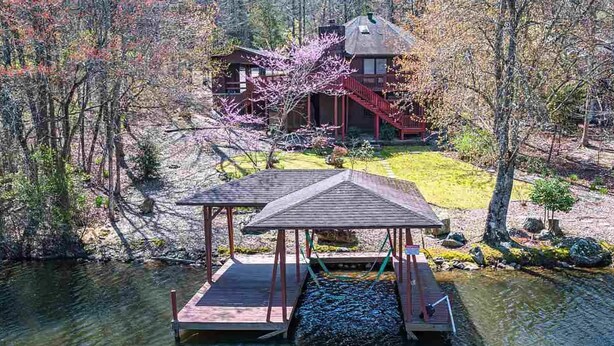 A wooden dock with a gazebo, a house with a red staircase, and a forested area with a river.