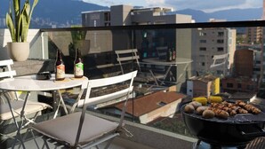 A balcony with a grill, two bottles, a potted plant, and a table with chairs. - Organic, Comfy & New loft in Laureles Quarter (Medellín)
