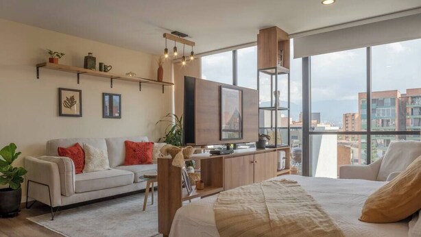 A modern bedroom with a large bed, a sofa, a TV, and a city view. - Organic, Comfy & New loft in Laureles Quarter (Medellín)