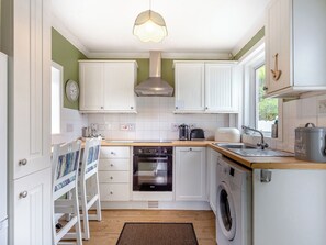 A compact kitchen with white cabinets, a wooden countertop, a built-in oven, a washing machine, and a hanging light fixture.