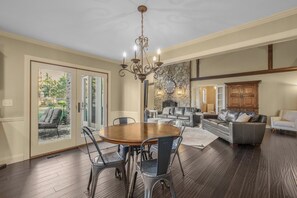 A spacious living room with a fireplace, a dining area with a chandelier, and a view through a glass door to an outdoor area.