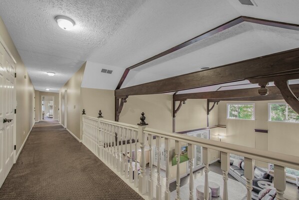 A spacious hallway with a carpeted floor, white railings, and wooden beams.