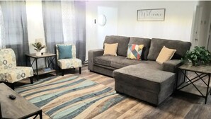 Un salon avec un canapé gris, un fauteuil à motifs et une petite table sur laquelle est posée une plante.