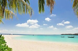 Ein Strand mit klarem türkisblauem Wasser, einem sandigen Ufer und einem Boot in der Ferne.
