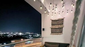 A balcony with a hanging chair, a sofa, and a small table. There is a view of a cityscape and a highway in the background. - A lavish hidden gem in the heart of Dubai marina. (Dubai)