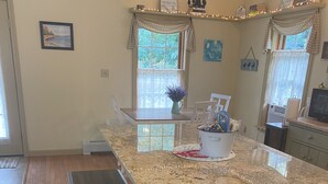 A kitchen with a granite countertop, wooden bench, and a window with curtains. - 20min from Acadia Retreat With Internet & Gaming Amenities (Hancock)