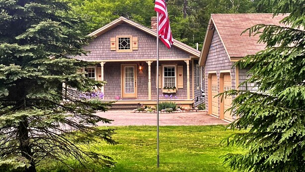 A two-story house with a front porch, a garage, and a flagpole with an American flag. - 20min from Acadia Retreat With Internet & Gaming Amenities (Hancock)