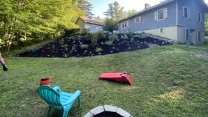 A residential backyard with a garden bed, a blue chair, and a red chair. - 20min from Acadia Retreat With Internet & Gaming Amenities (Hancock)