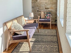 A cozy seating area with a woven sofa and a chair, a patterned rug, and a stone wall in the background. - 3 bedroom accommodation in Kettlewell (Kettlewell)