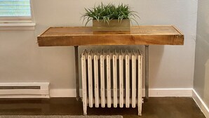 Una sala de estar con un televisor montado, una mesa consola de madera con una planta y un radiador blanco.