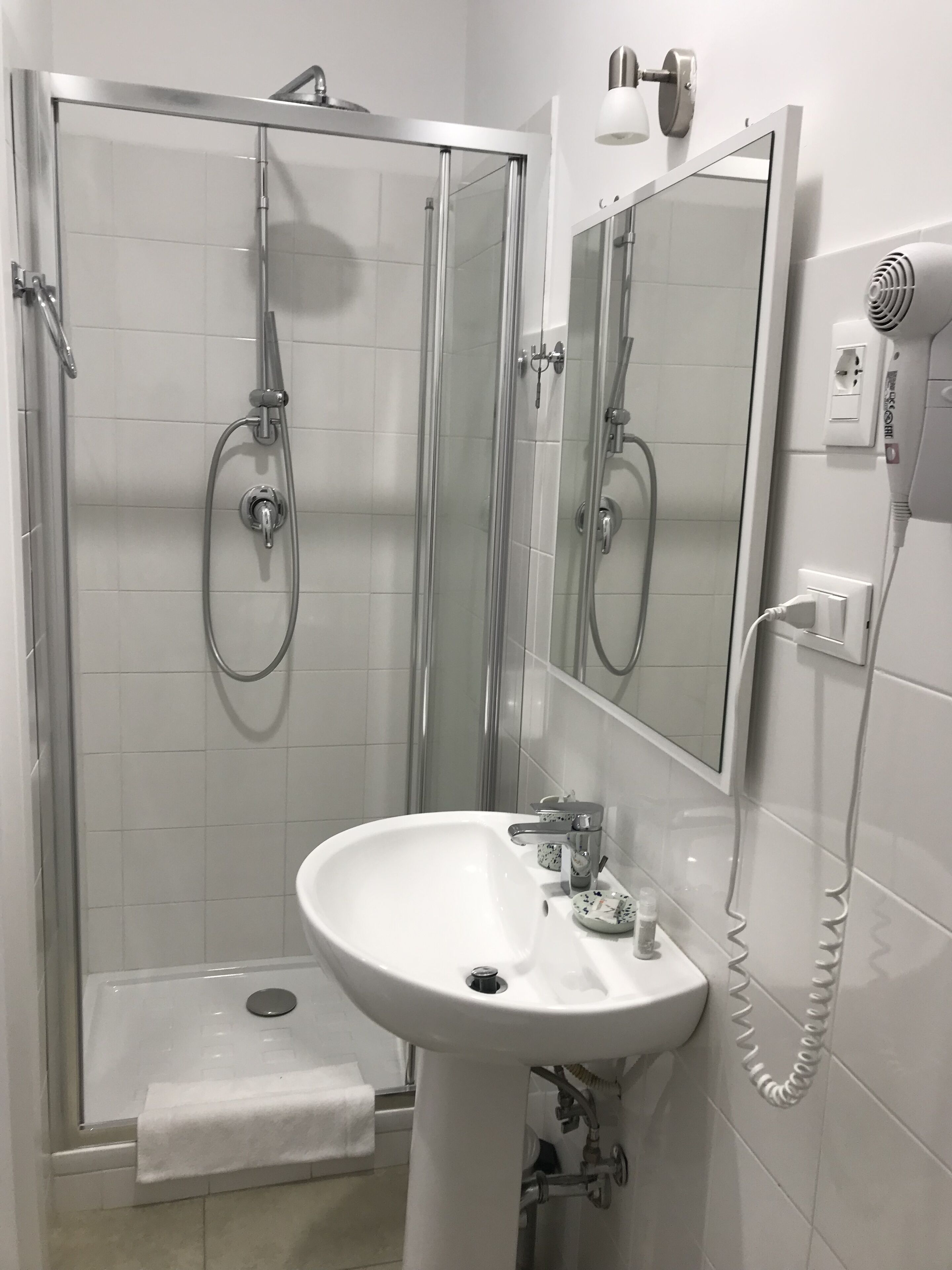 Een moderne badkamer met een douchecabine van glas, een wastafel op voet en een spiegel.