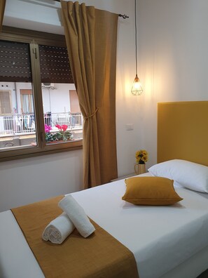 A hotel room with a bed, a window with curtains, a wall-mounted light fixture, and a view of the outside balcony. - Affittacamere Dianir (Rome)