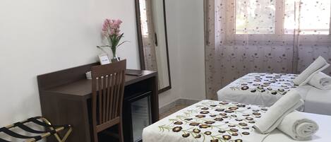 A hotel room with a bed, a desk, a chair, a TV, and a window with floral curtains.