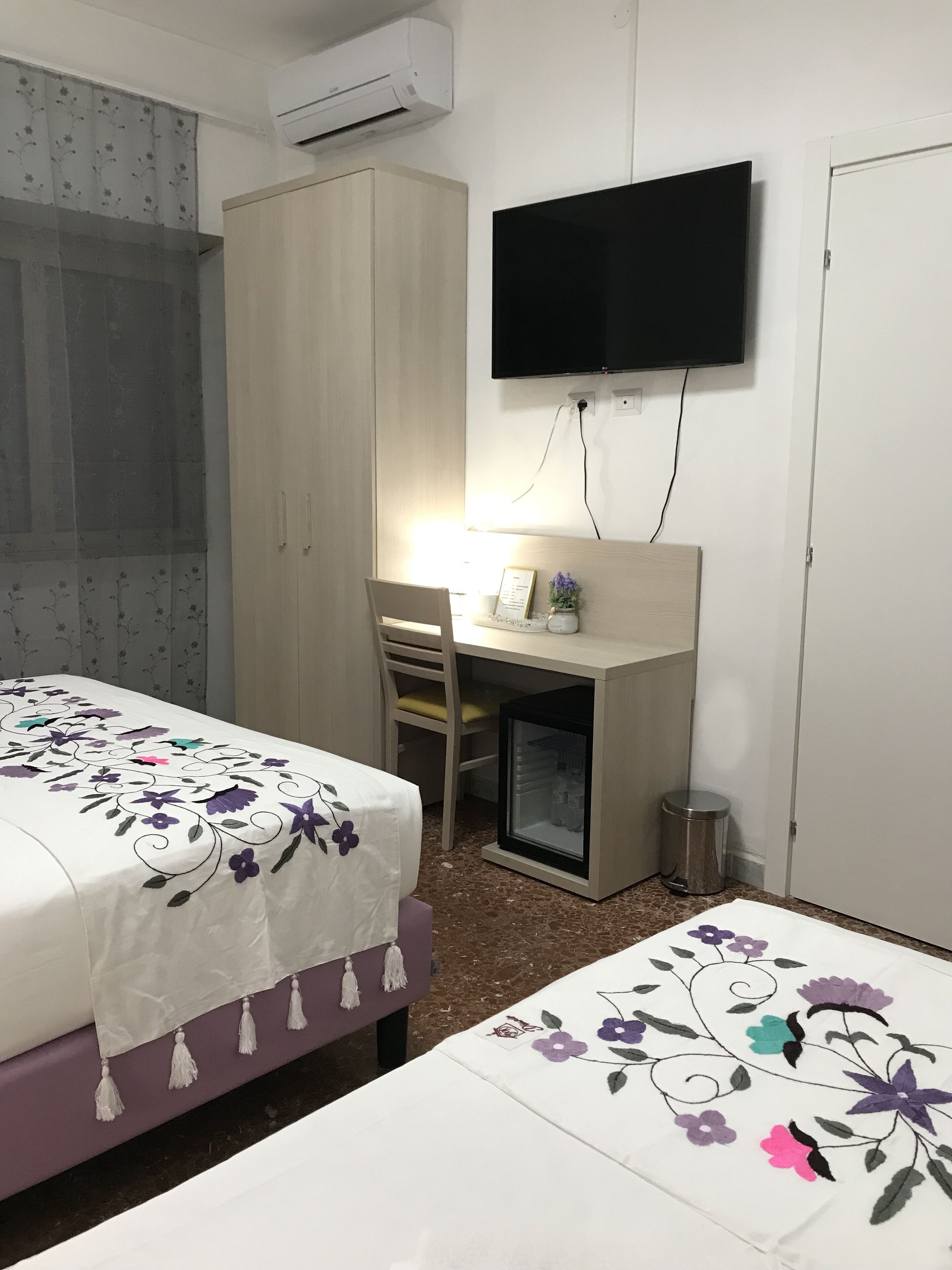 A hotel room with a bed, a desk with a chair, a television, and a wardrobe.