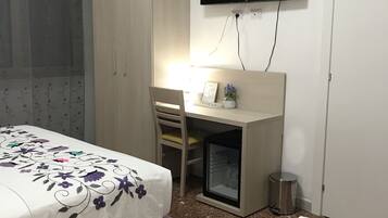 Una habitación de hotel con cama, un escritorio con silla, televisor y armario.