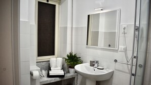 A bathroom with a white sink, a mirror, a towel rack, a potted plant, and a shower. - Affittacamere Dianir (Rome)