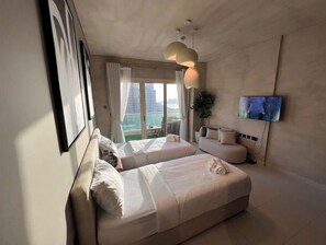 Quarto de hotel com duas camas, televisão e varanda com vista para a cidade.