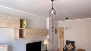A modern living room with a flat-screen TV, wooden shelves, a lamp, and a chair.