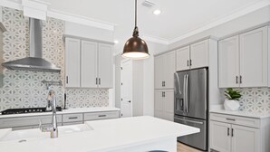 Eine moderne Küche mit weißen Schränken, einem Edelstahlkühlschrank und einer zentralen Kochinsel mit Sitzgelegenheiten.