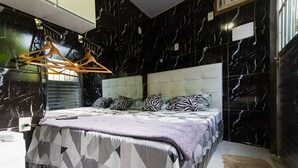 A bedroom with a black marble wall, a tufted headboard, a geometric-patterned bedspread, and zebra-print pillows. - Barra da Tijuca Guest Houses (Rio de Janeiro)