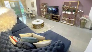Olohuoneessa on tummansininen sohva, pyöreä sohvapöytä ja televisio puisen jalustan päällä. Taustalla näkyy ruokailutila, jossa on pöytä ja tuolit.