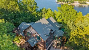 Una cabaña con techo inclinado, rodeada de un bosque frondoso y con vista a un lago.