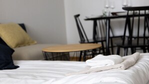 A neatly made bed with a beige blanket, a small table with chairs, and a wall clock. - 2ndhomes Central 1BR Apartment w Balcony (Helsinki)