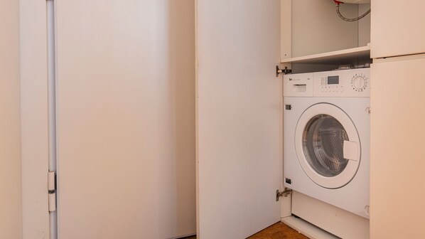 A closed door with a white wall and a washing machine in the corner.