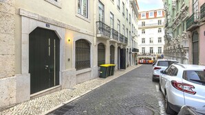 A narrow cobblestone street lined with historic buildings, parked cars, and a tram in the background. - Central Downtown Apartment by LovelyStay (Lisboa)