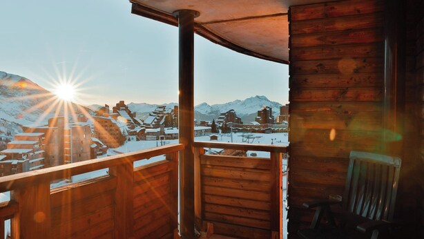 Eine Holzhütte mit Balkon mit Blick auf ein verschneites Bergdorf.