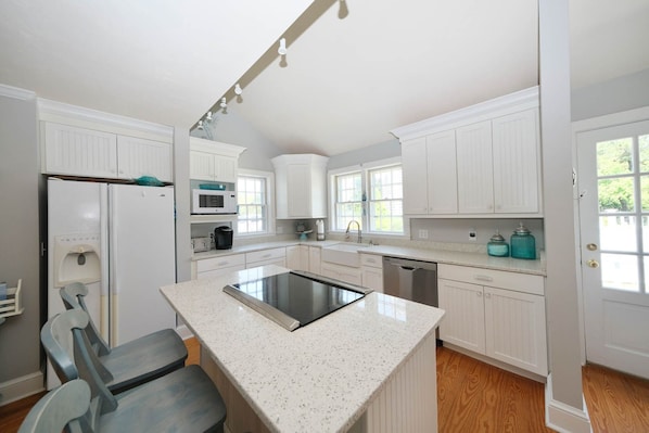 A modern kitchen with white cabinetry, a central island with a stovetop, and a dishwasher.