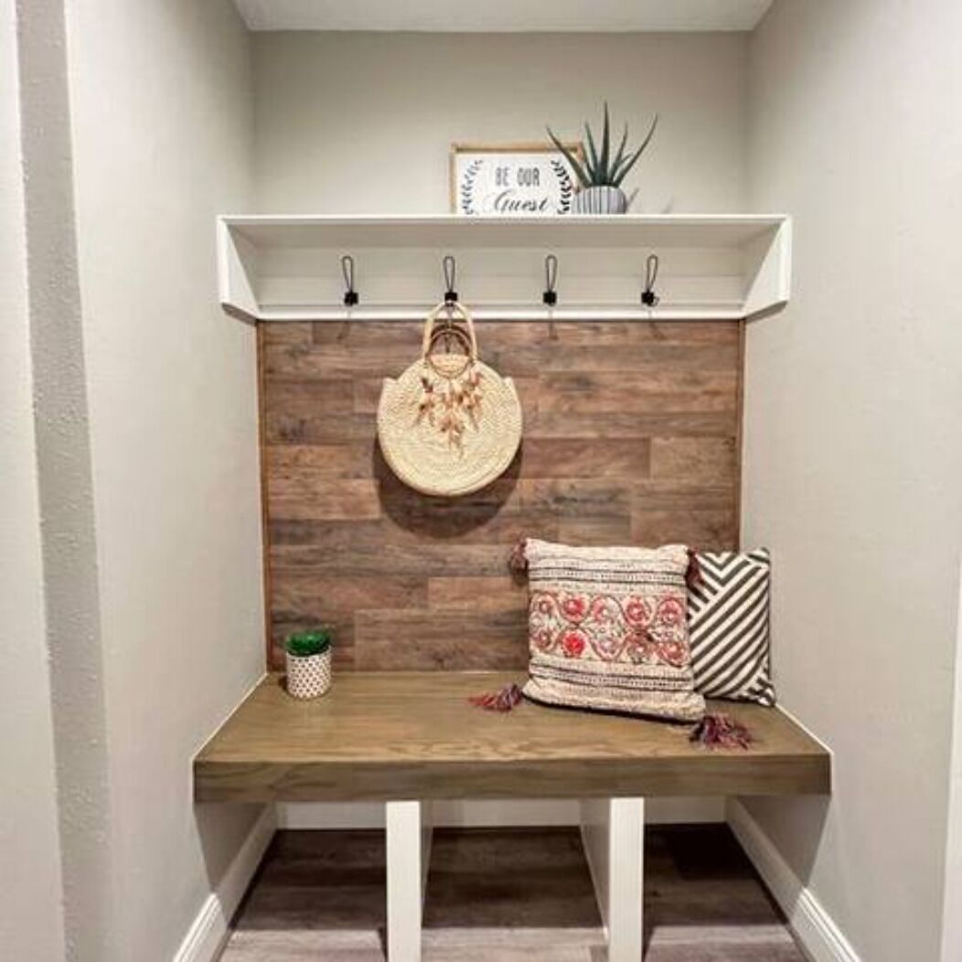 A wooden bench with a woven bag hanging on a metal hook, a small potted plant, and a cushion with a geometric pattern.