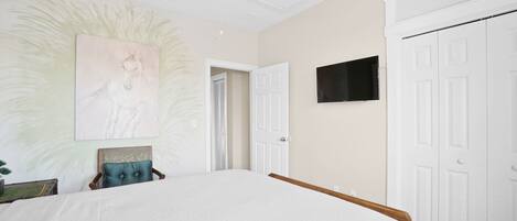 A bedroom with a bed, a ceiling fan, a TV, and a door.