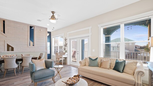 A spacious living room with a beige sofa, a round coffee table, and a dining area with a table and chairs. - Beach House - Dreams Come True by PHG (Panama City Beach)