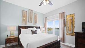 A bedroom with a large bed, a nightstand, a dresser, a ceiling fan, and a window with curtains. - Beach House - Dreams Come True by PHG (Panama City Beach)