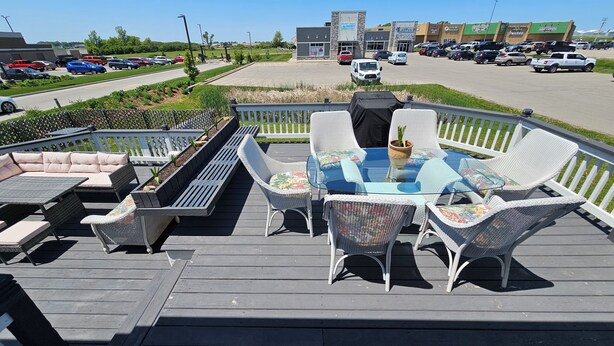 An outdoor deck with wicker furniture, a glass-top table, and a view of a parking lot and buildings in the background. - This big old charming house Viroqua (Viroqua)