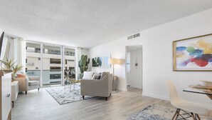 A modern living room with a sofa, a dining table, and a large window. - Stunning ocean front unit 2/2 with privet beach excess (Hollywood)