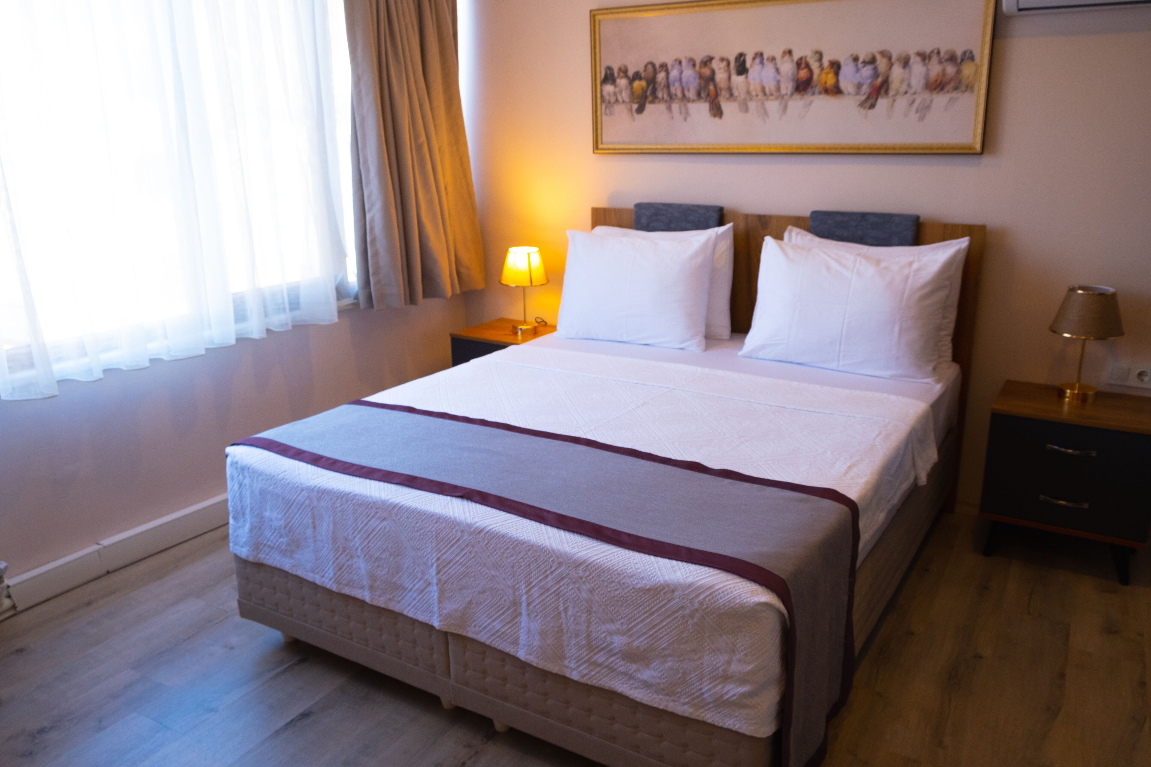A hotel room with a large bed, two bedside tables, a lamp, a framed picture on the wall, and a window with curtains.
