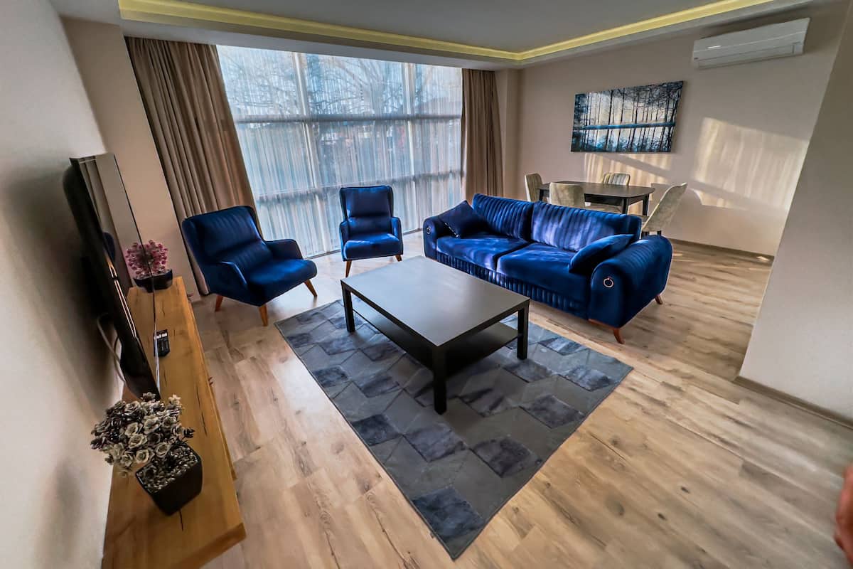 Un salon moderne avec un canapé bleu, deux fauteuils, une table basse et un téléviseur.