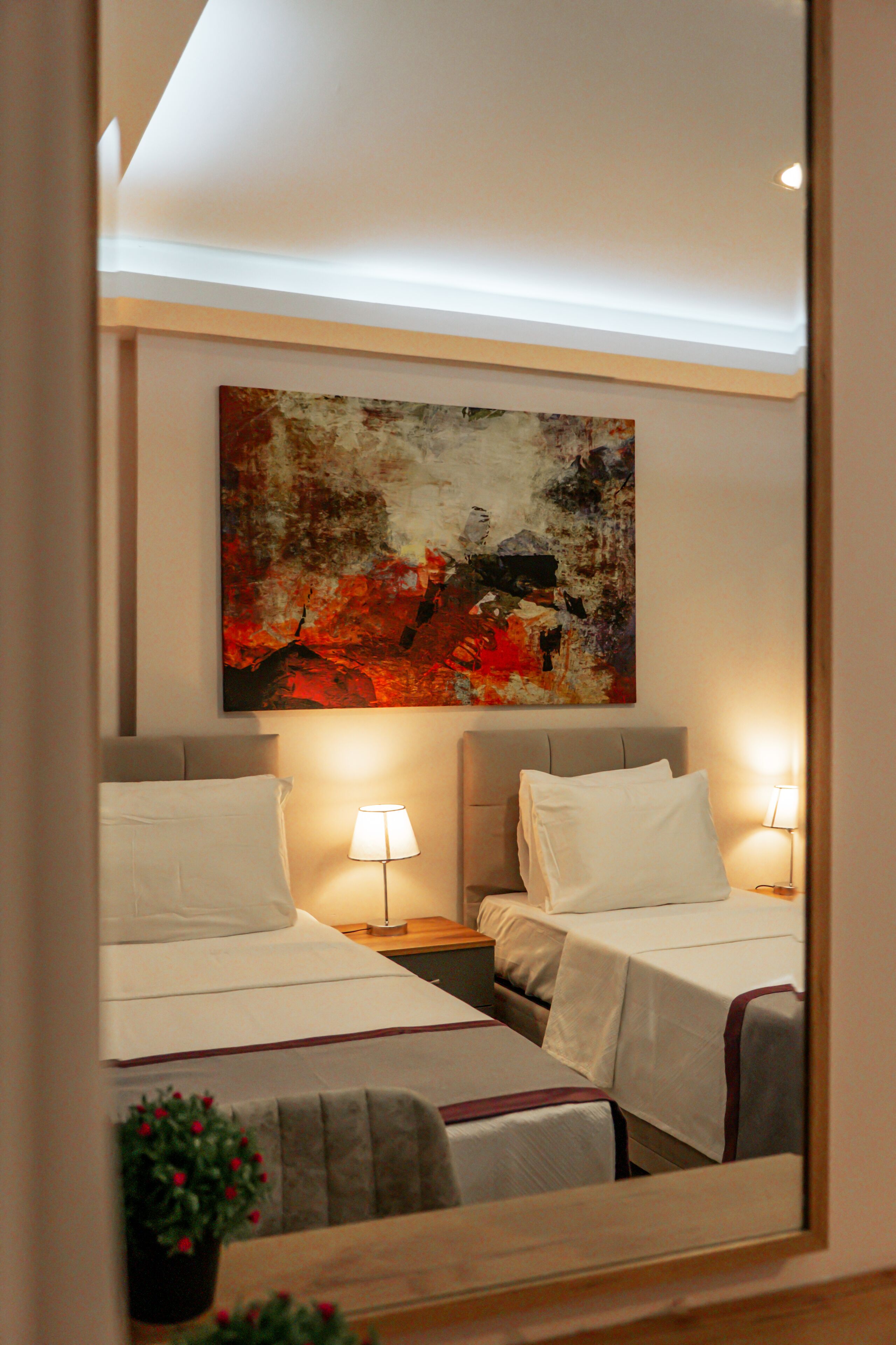 A hotel room with two beds, bedside lamps, a large abstract painting on the wall, and a small potted plant.