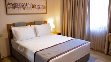 A neatly made bed with white linens and a red accent, a bedside lamp, and a framed bird painting on the wall.