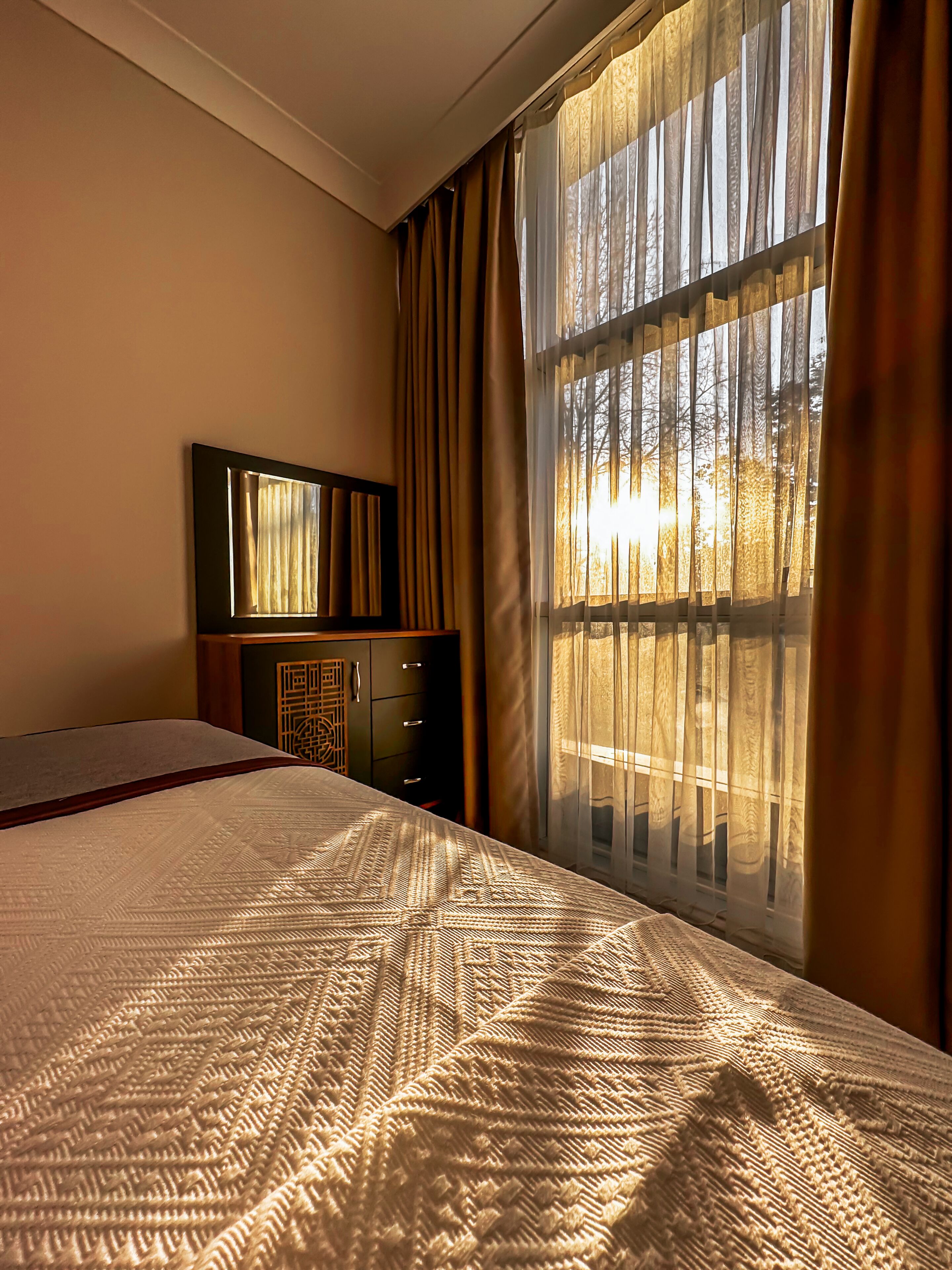 Een hotelkamer met een groot bed, een dressoir en een raam met gordijnen.