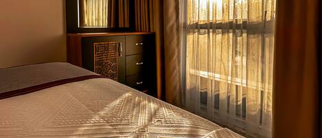 Een hotelkamer met een groot bed, een dressoir en een raam met gordijnen.