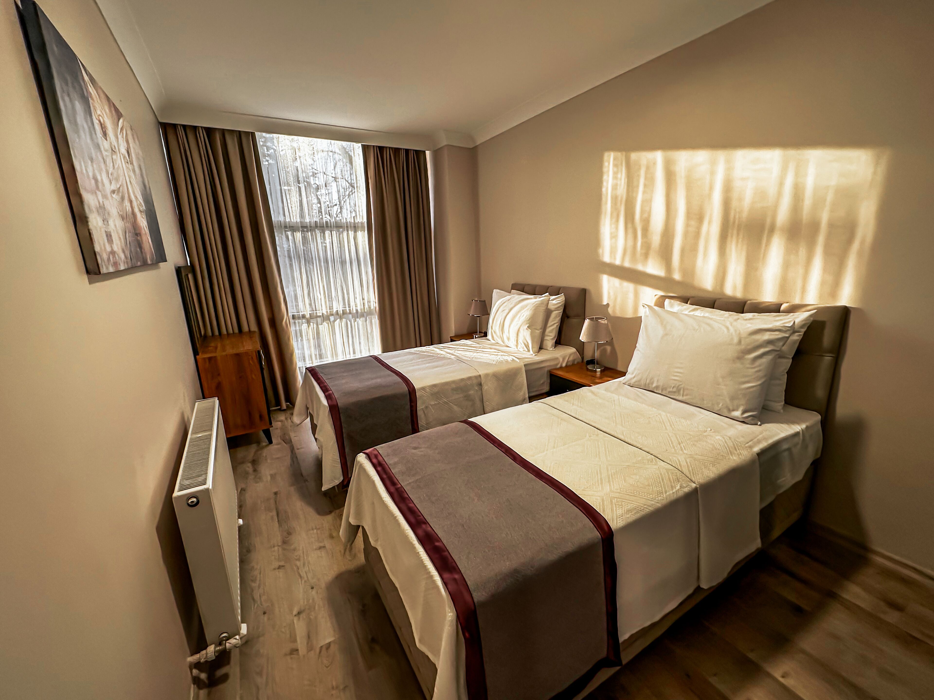 Habitación de hotel con dos camas, un radiador, una ventana con cortinas y suelo de madera.