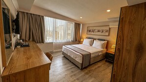 Una habitación de hotel moderna con una cama grande, un escritorio de madera, un radiador y una ventana con cortinas.
