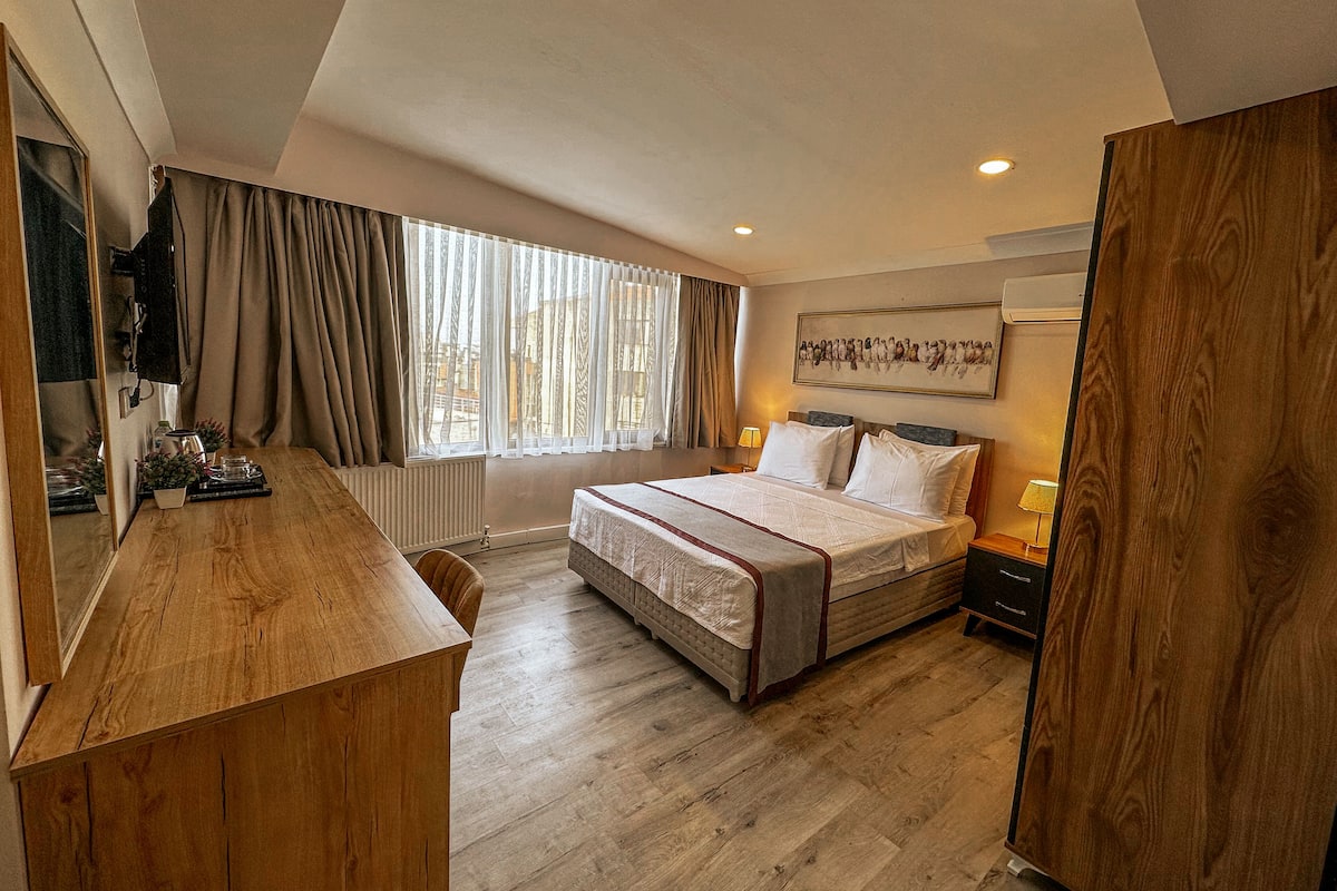 Une chambre d’hôtel moderne avec un grand lit, un bureau en bois, un radiateur et une fenêtre avec des rideaux.