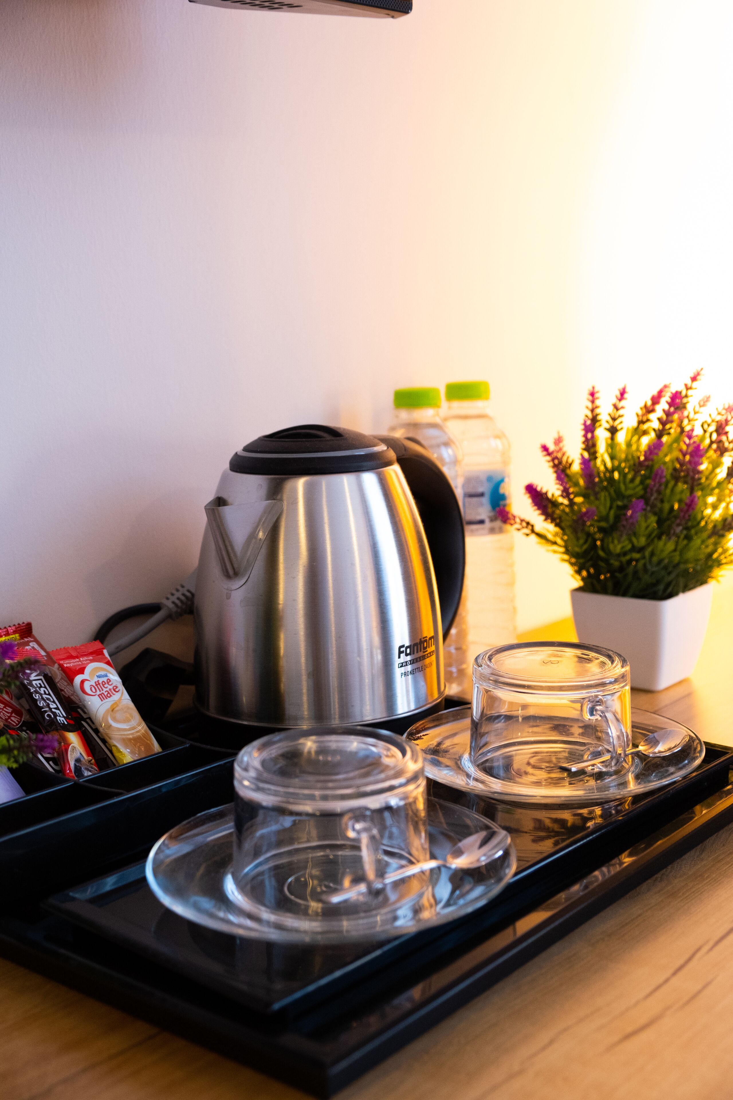 Un plateau contenant une cafetière, deux bouteilles d’eau, un verre et un sachet de crème pour café.